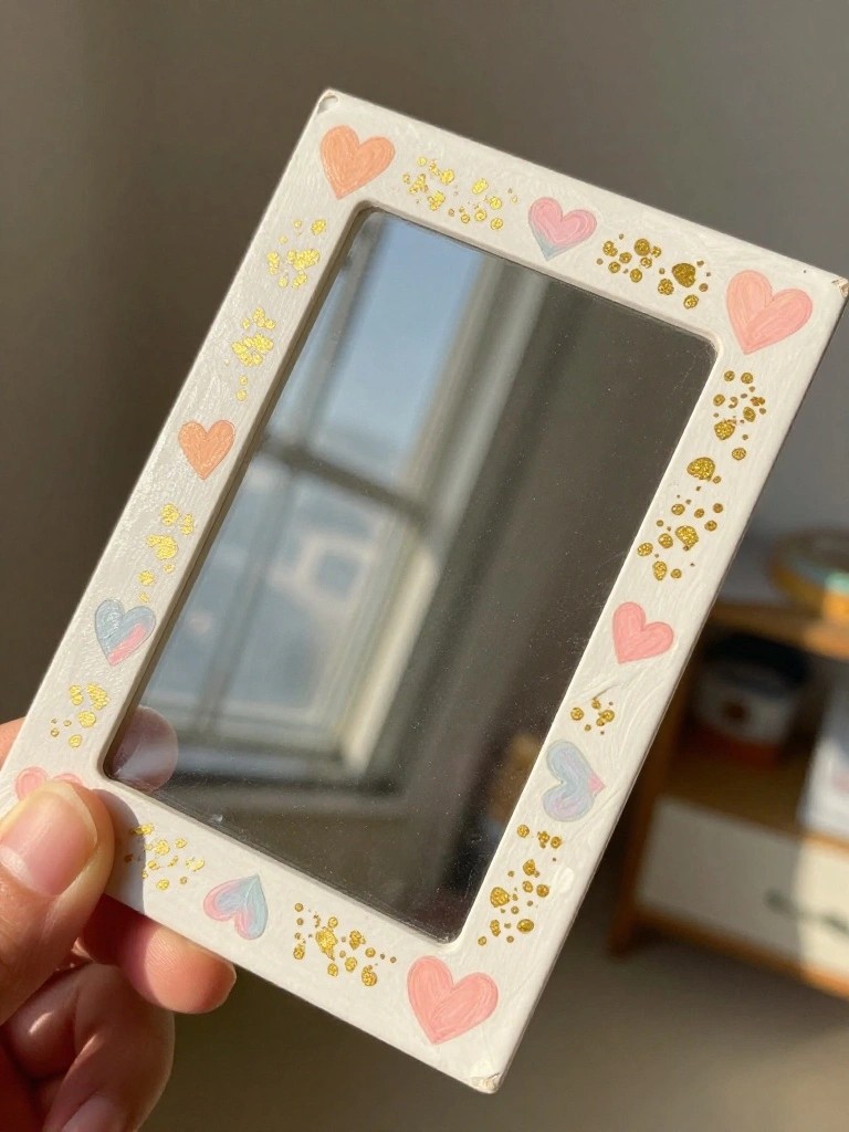 Hand holding white mirror frame decorated with pink hearts and gold glitter dots