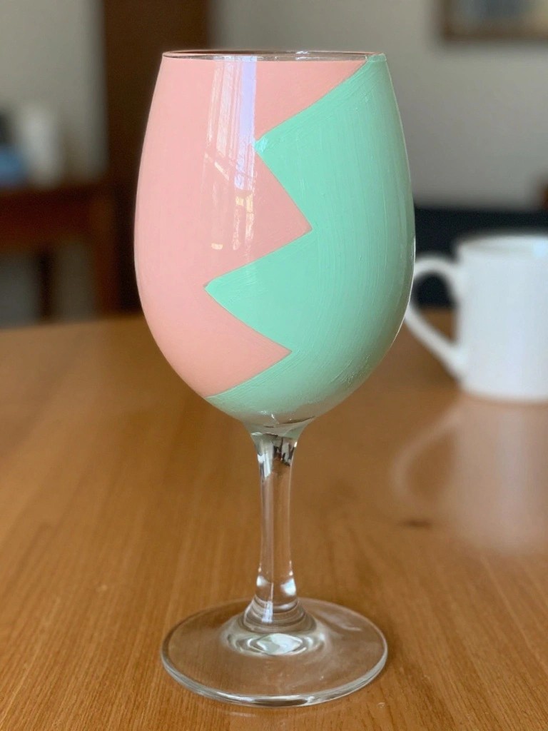 Pink and mint green zigzag-painted wine glass on wooden table.