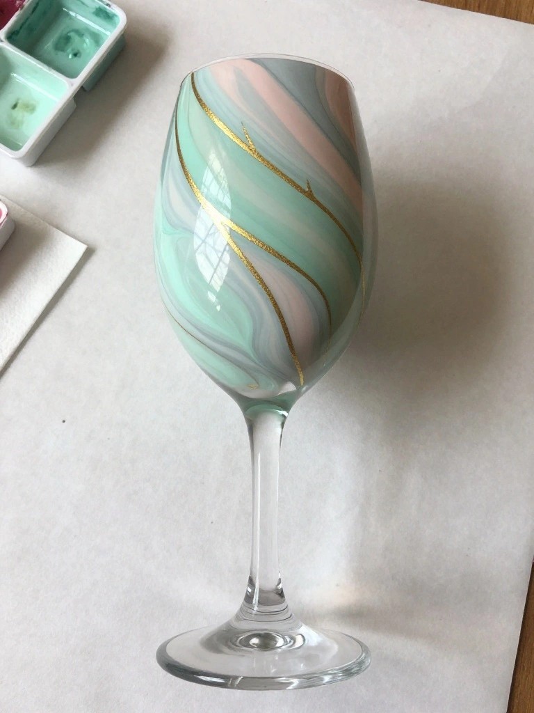 Marbled mint green and pink wine glass with gold accents beside paint palette