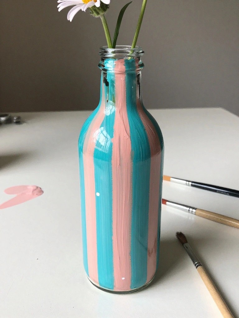 Pink and turquoise striped bottle with flower beside paintbrushes on white table
