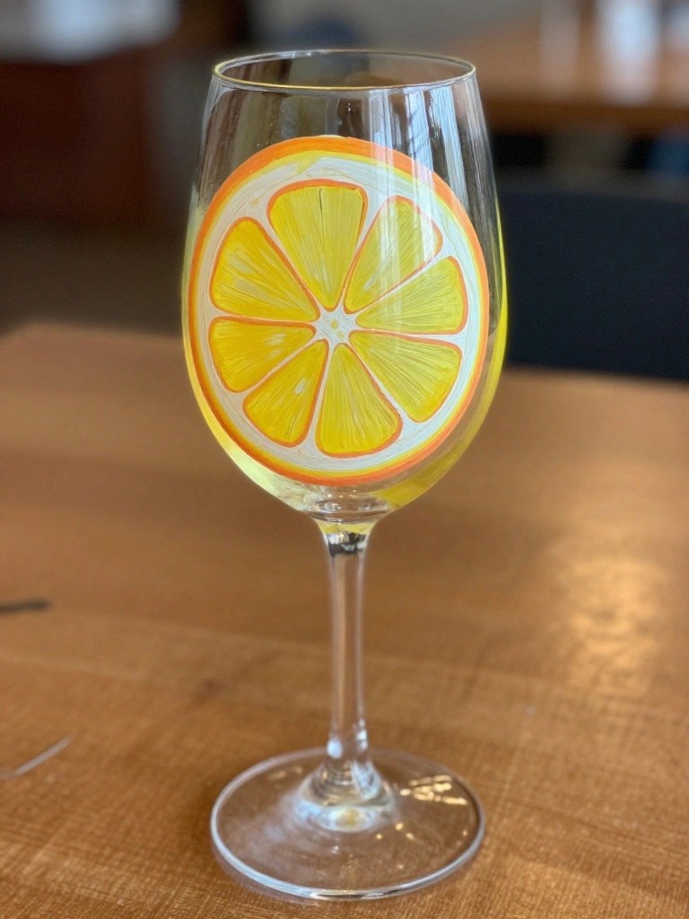 Wine glass with vibrant yellow lemon slice painting on wooden table