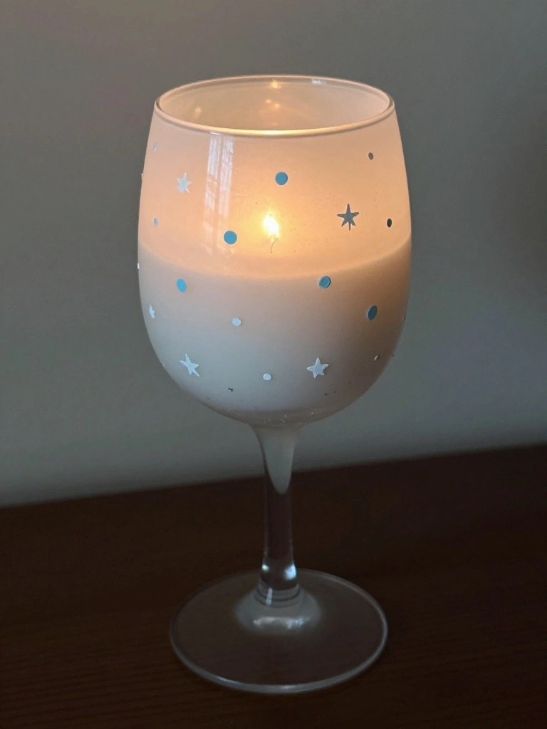 Lit candle in wine glass with blue and white star and dot decorations