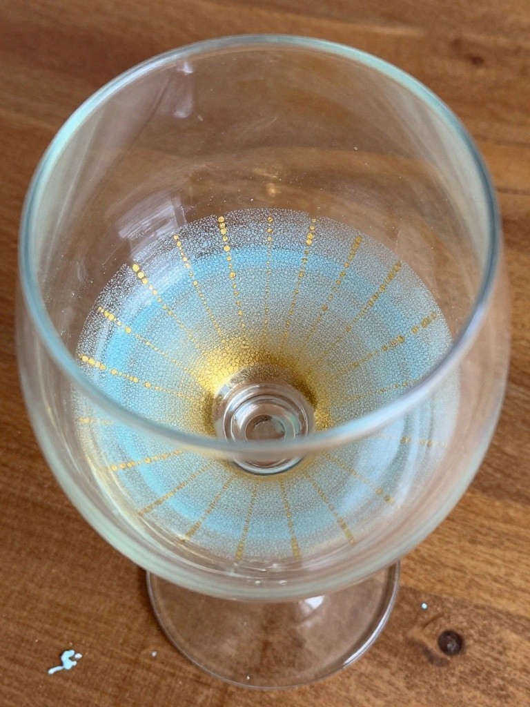 Clear wine glass with light blue and gold dotted radial pattern viewed from above