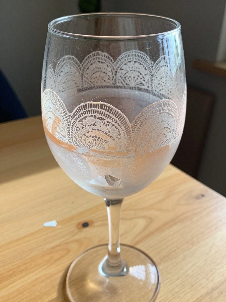Clear wine glass with etched lace pattern and orange smudges on wooden table