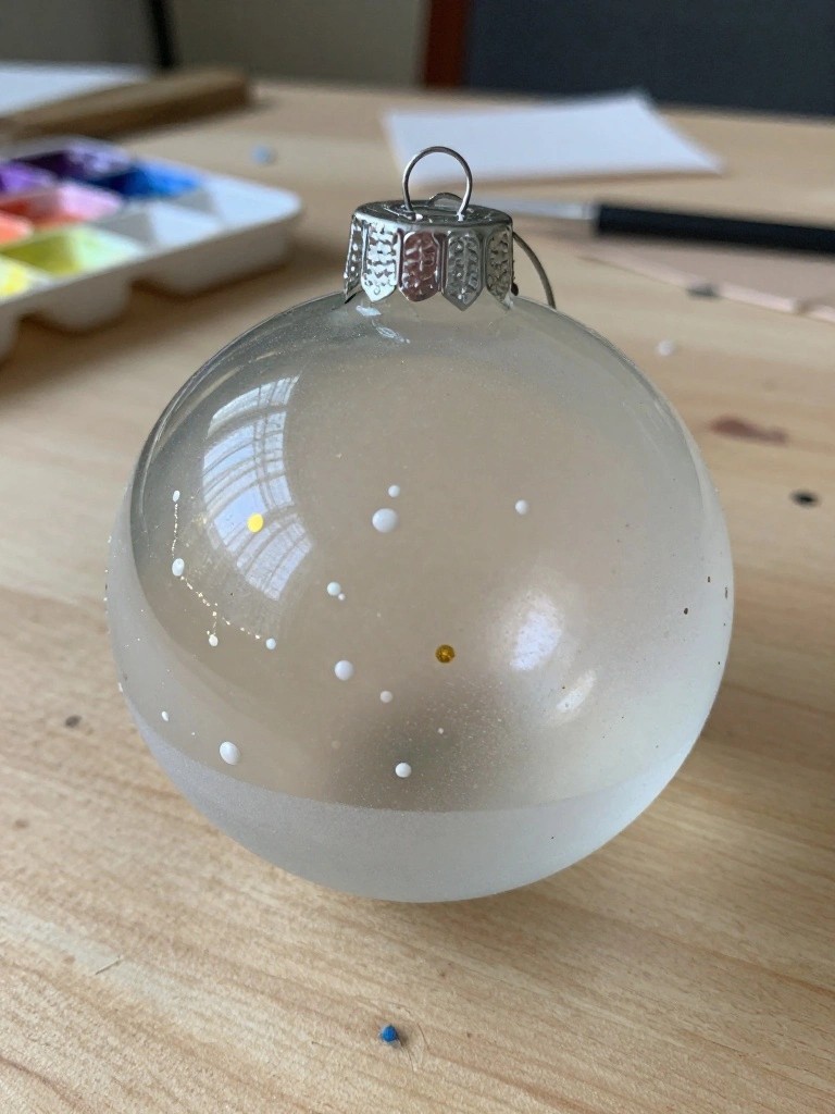 Glass Christmas ornament with white and gold dots on wooden table