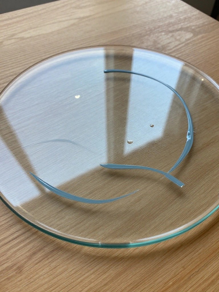 Broken light-blue ring pieces on transparent glass plate over wood grain.