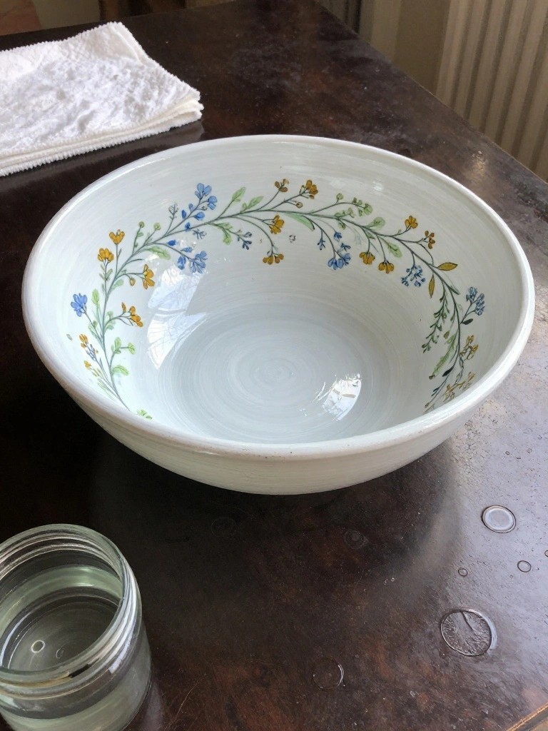 White ceramic bowl with blue-yellow floral vines on dark wooden table