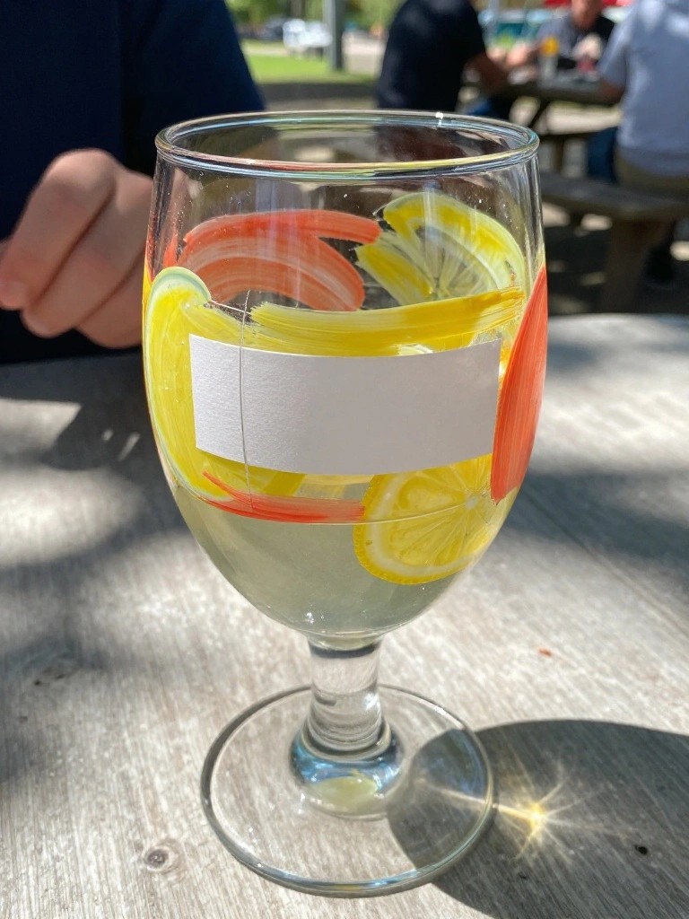Stemmed glass with yellow-orange brushstrokes, lemon slices, and white label on table