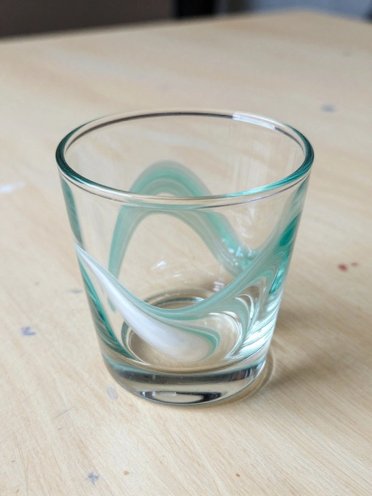 Clear glass tumbler with swirling teal and white patterns on wooden table