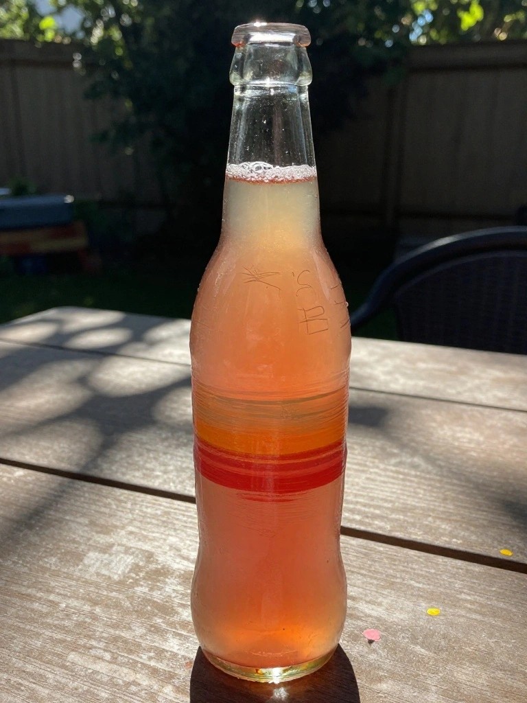 Glass bottle of layered orange liquid with red stripe on wooden table