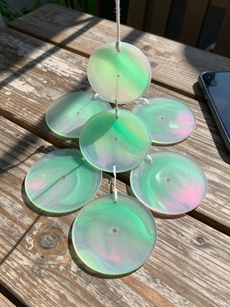 Iridescent green and pink circular discs strung into a hanging mobile on wood