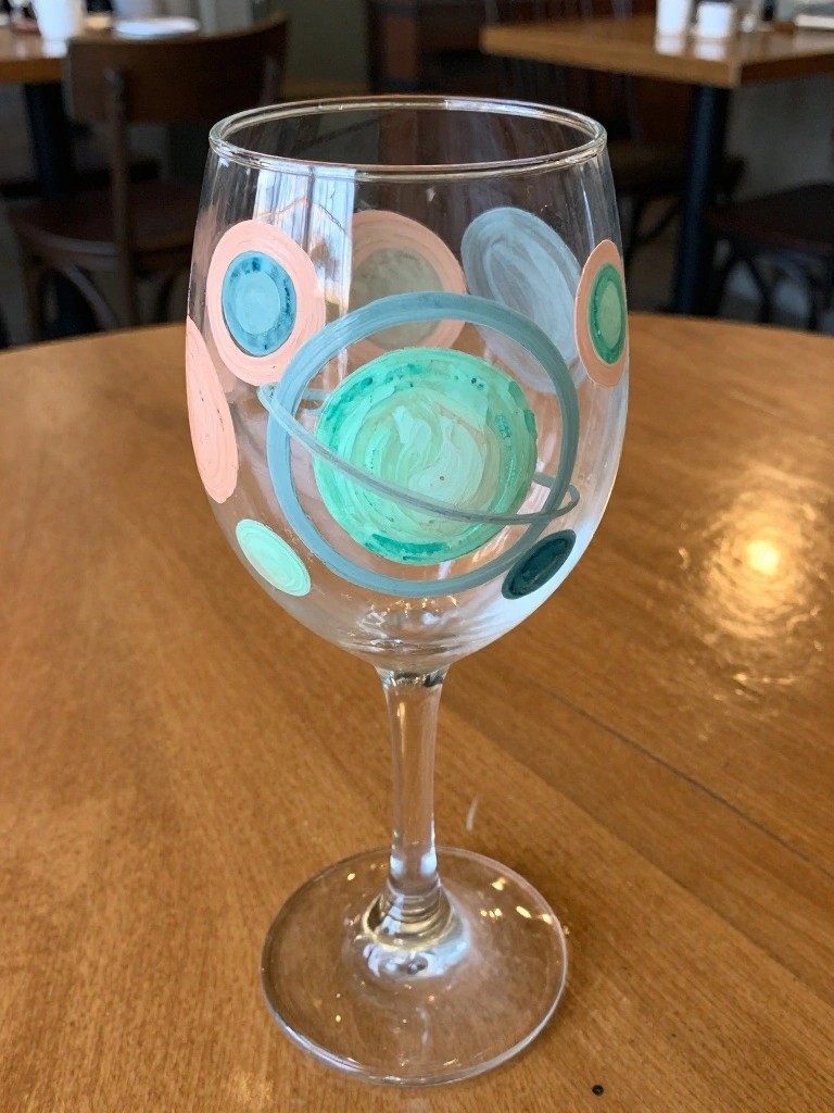 Decorated wine glass with teal planet rings and pastel circles on wooden table