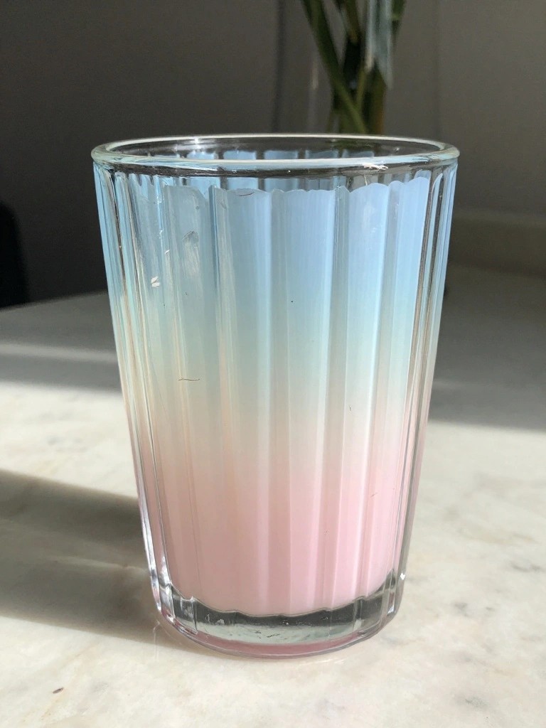 Ribbed glass tumbler with blue-to-pink gradient on marble surface