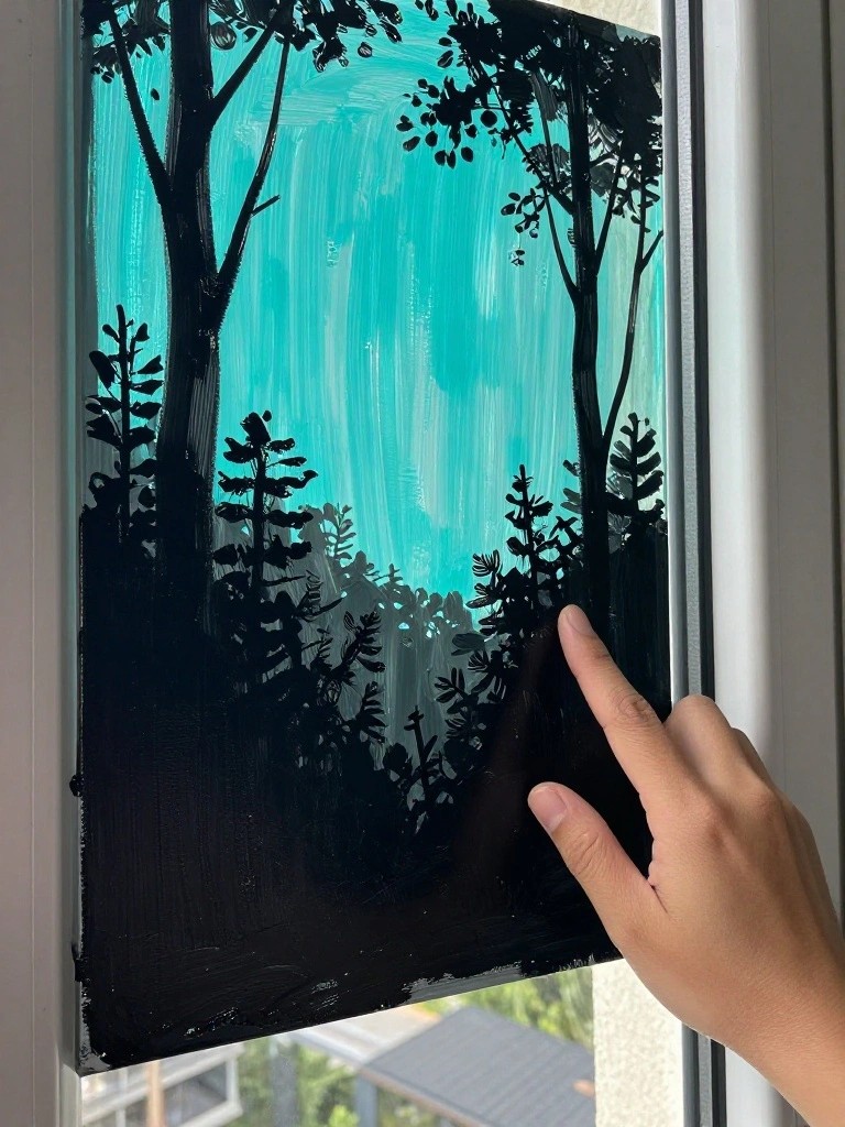 Hand touching black tree silhouettes on turquoise canvas painting by window