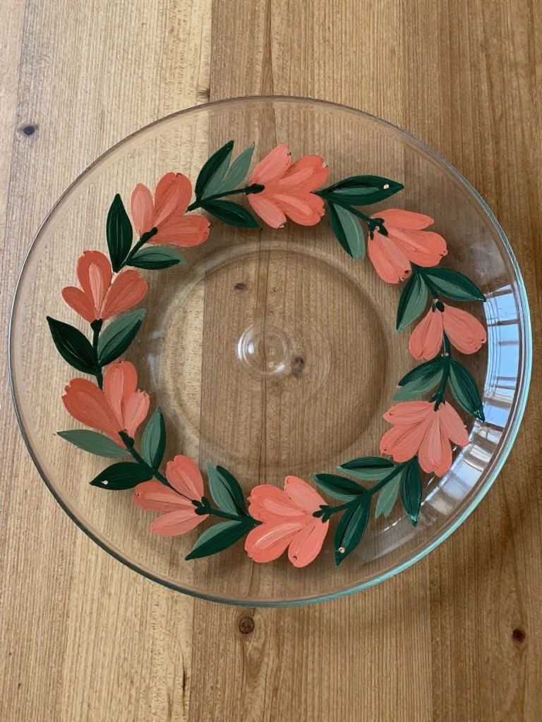 Clear glass bowl with painted coral flowers and green leaves on wood.