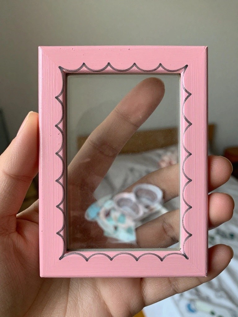 Hand holding pink scalloped mirror frame reflecting finger and plush toy.