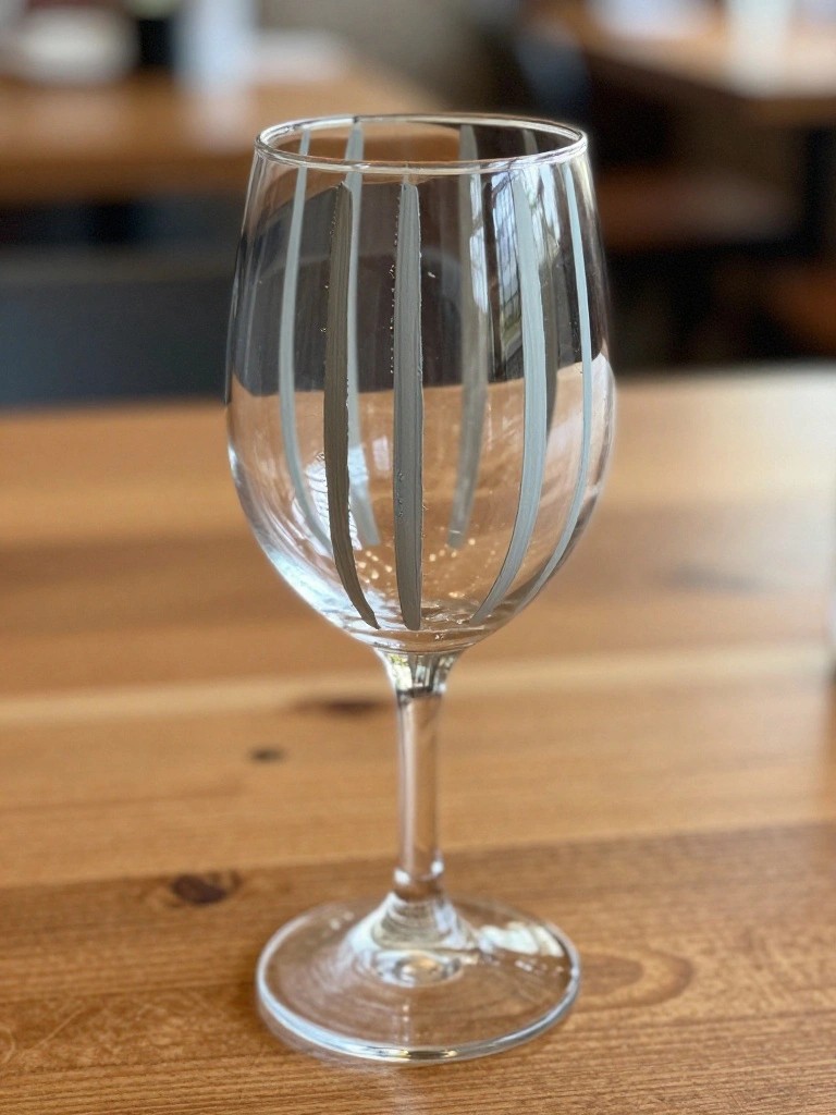 Stemmed wine glass with gray vertical stripes on wooden table with droplets