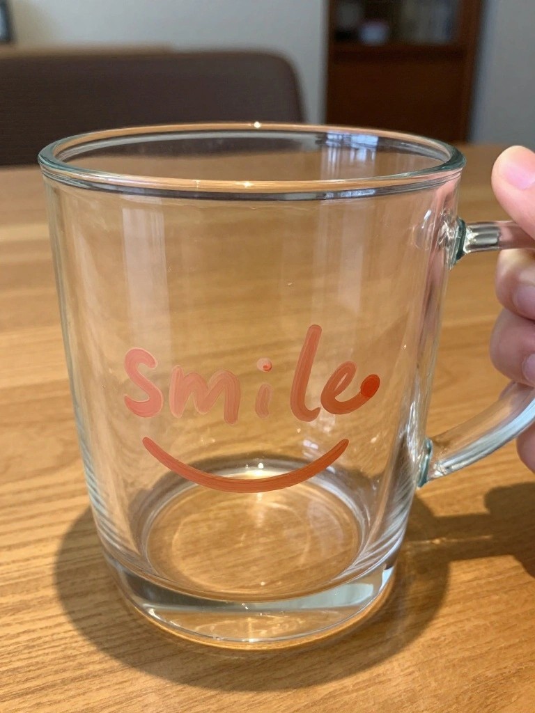 Clear glass mug with orange smile text held by hand on wooden table