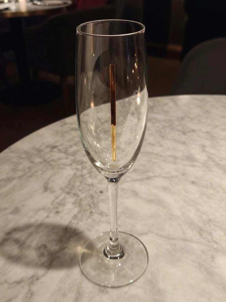Tall clear champagne flute with vertical matchstick on white marble table