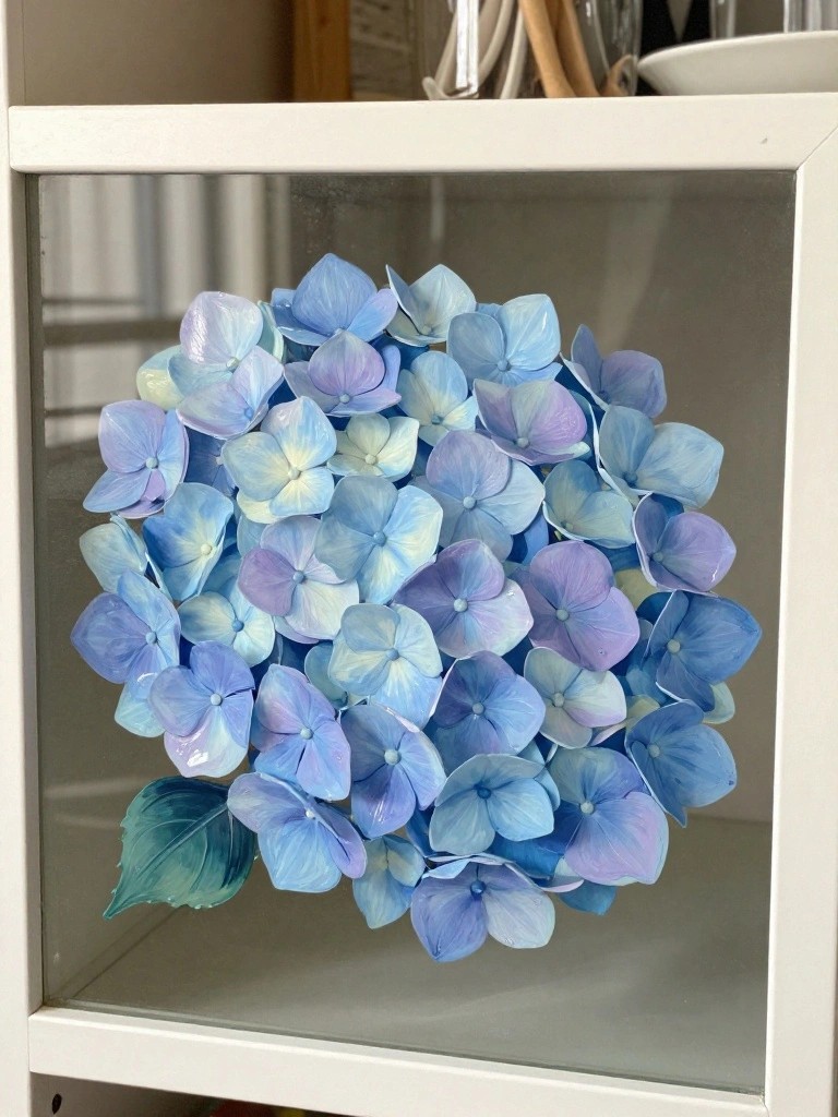 A cluster of blue and purple hydrangea flowers with one green leaf painted on the inside of a white cabinet glass door.