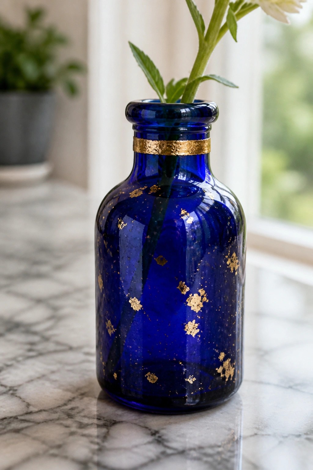 Deep blue glass vase with gold foil accents holding white flower on marble