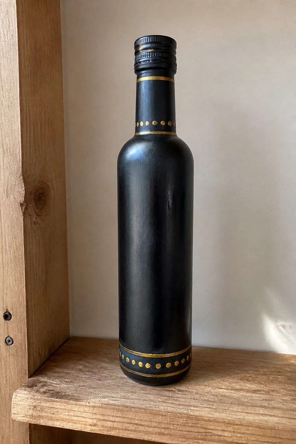 Black bottle with gold lines and dotted patterns on wooden shelf.