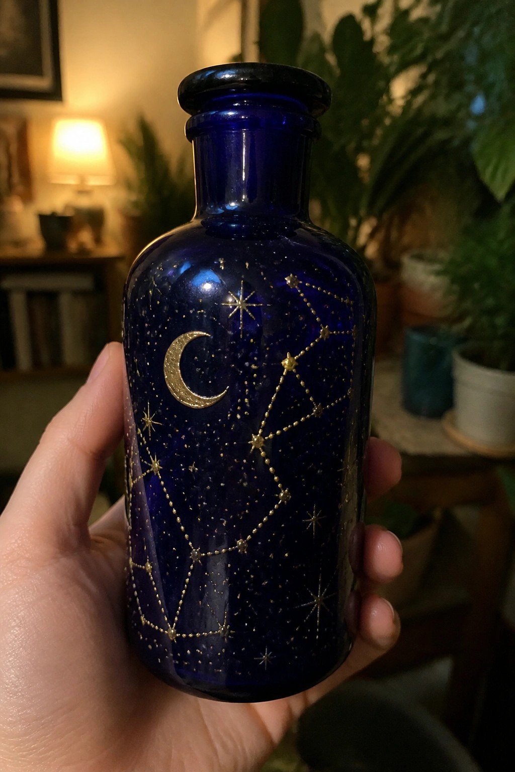 Hand holding cobalt blue bottle with gold moon, stars, and constellations