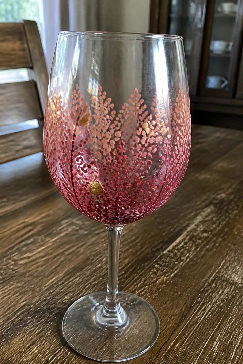 Decorated wine glass with red and gold dotted branches on wooden table
