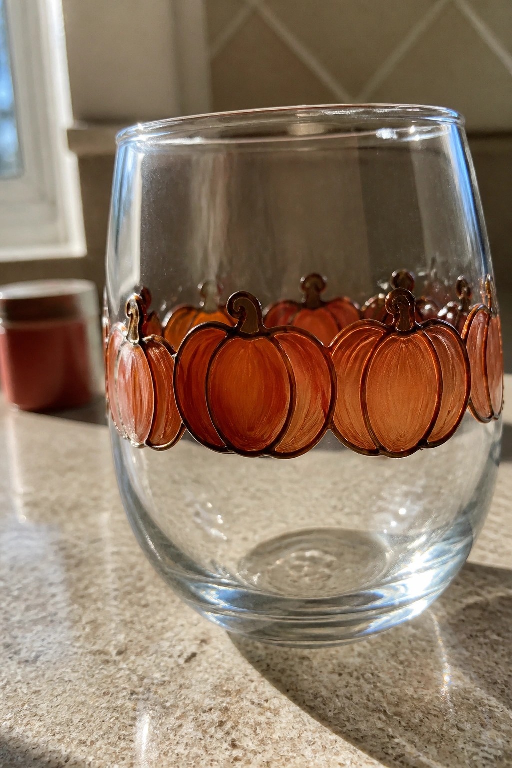 Clear stemless glass with orange pumpkin illustrations on marble countertop