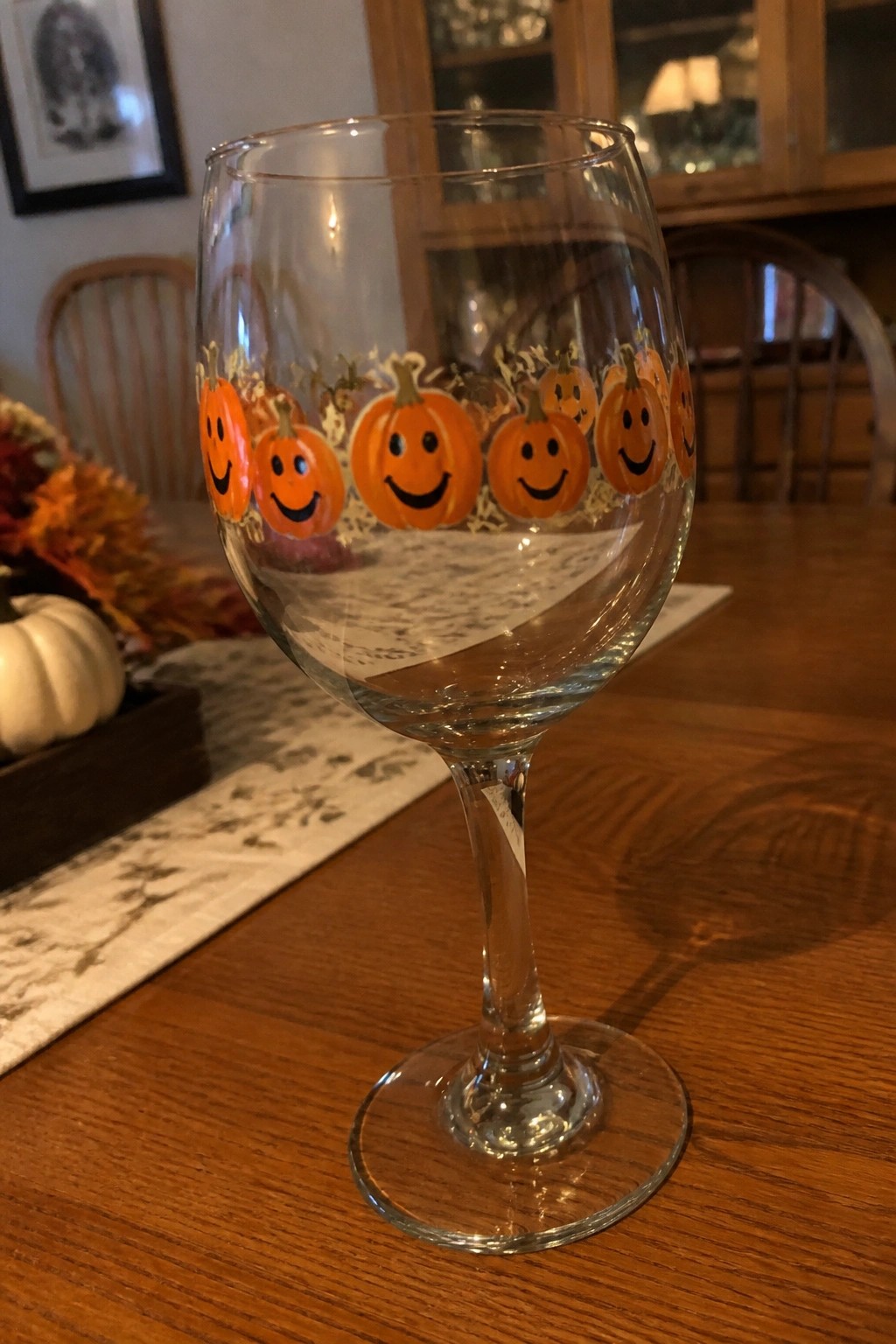 Wine glass with smiling orange pumpkins around bowl on wooden table