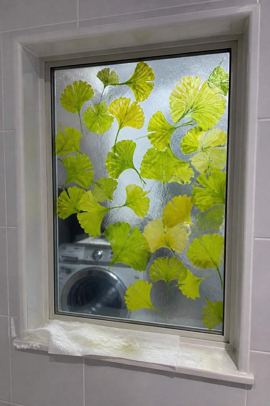 Window with vibrant green and yellow painted ginkgo leaves on frosted glass