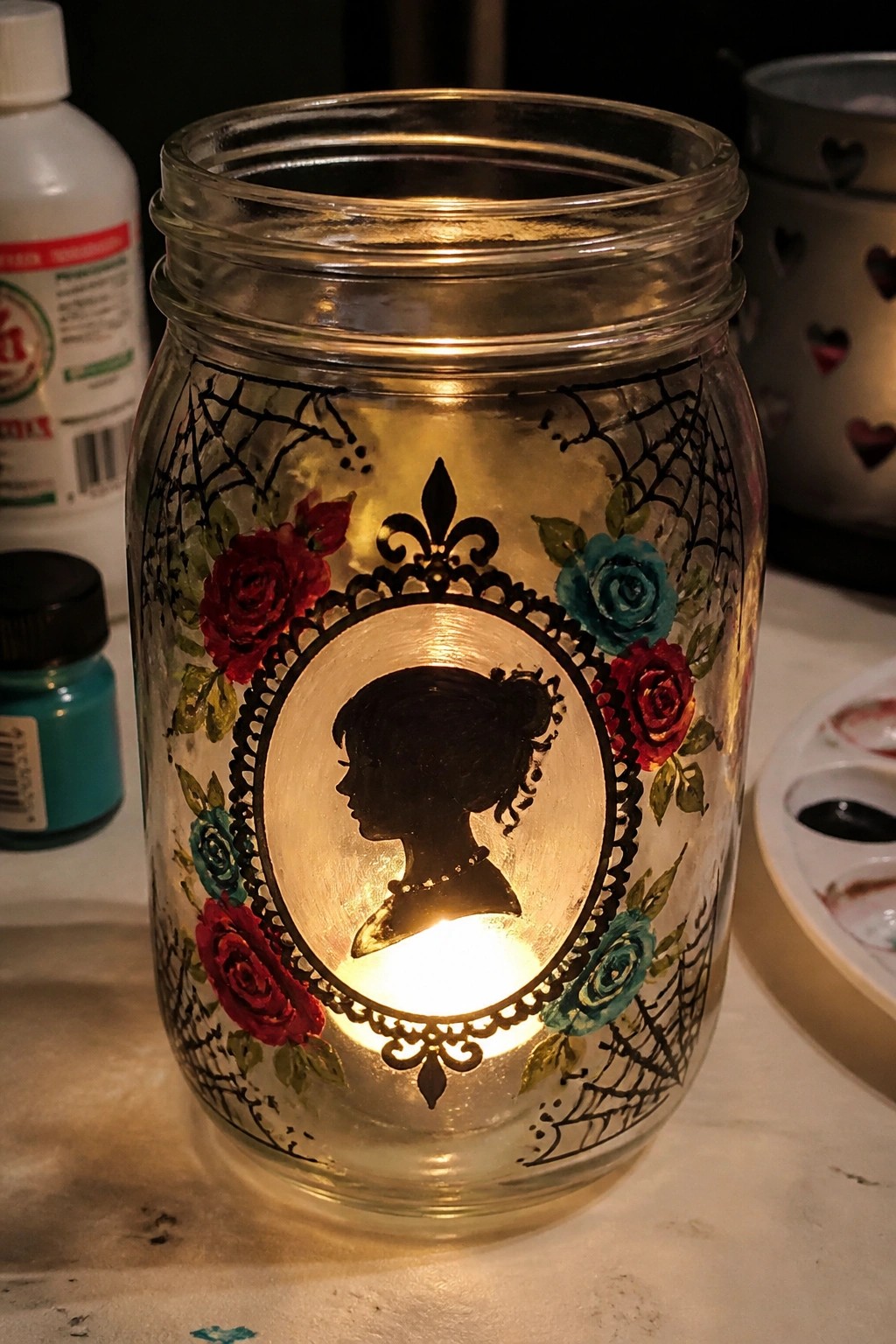 Glowing mason jar with black silhouette, red roses, teal flowers, and spiderwebs.
