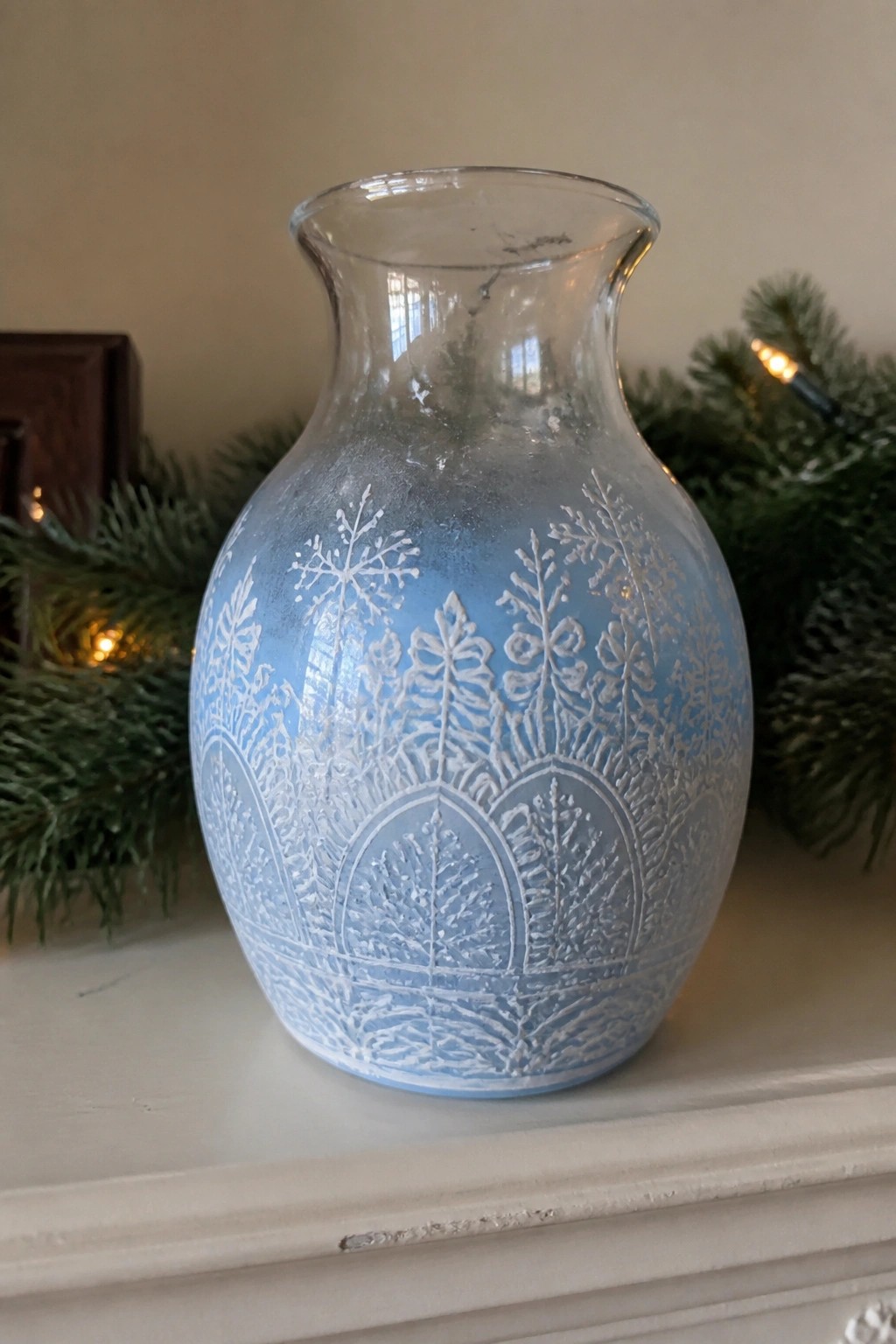 Blue frosted glass vase with etched snowflakes and trees on white mantel