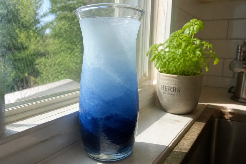 18 Elegant Winter Painted Vase Ideas Using Frosted Blue Gradient Effects Blue gradient glass vase on windowsill beside potted basil plant