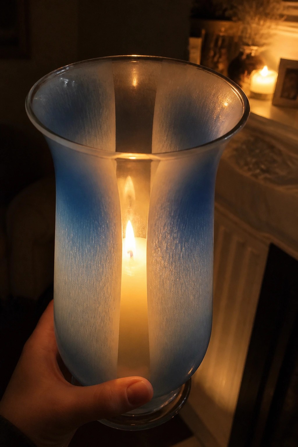 Hand holding blue frosted glass lantern with lit white candle inside