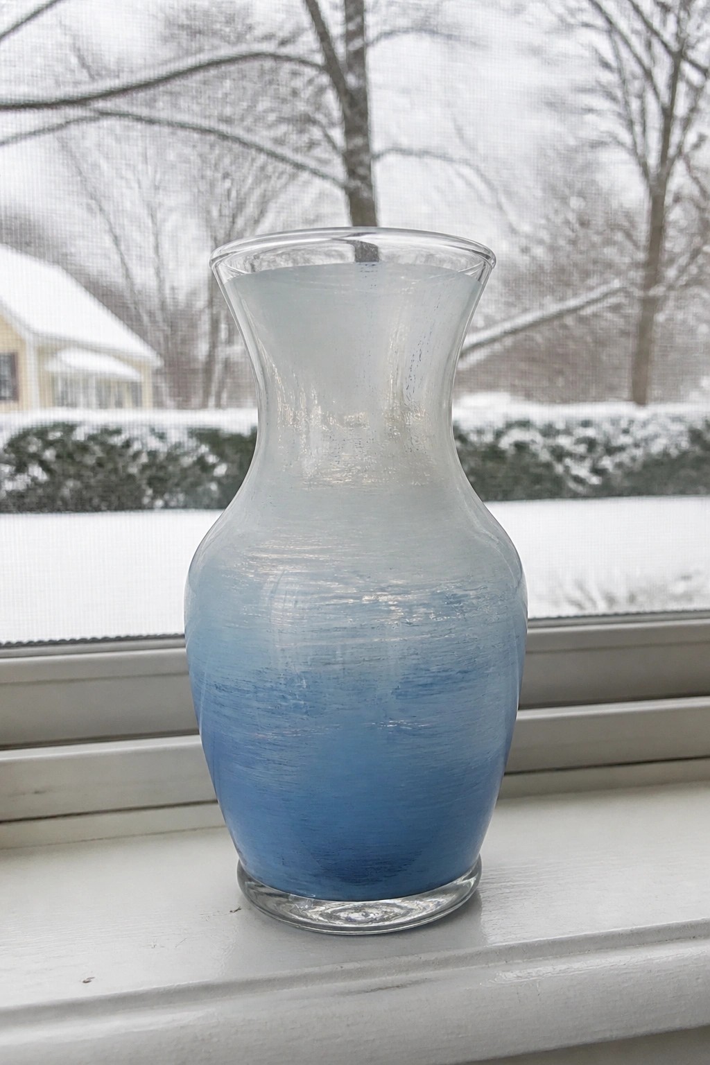 Frosted glass vase with blue gradient on white windowsill overlooking snowy scene