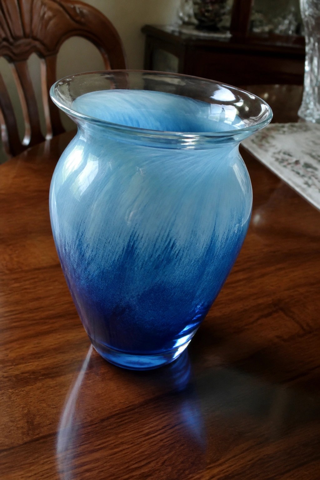 Blue swirled glass vase on polished wooden table with chair behind