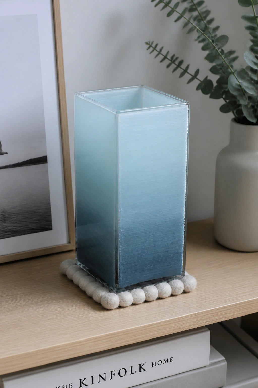 Blue gradient square glass vase on white felt pom-pom coaster on wood