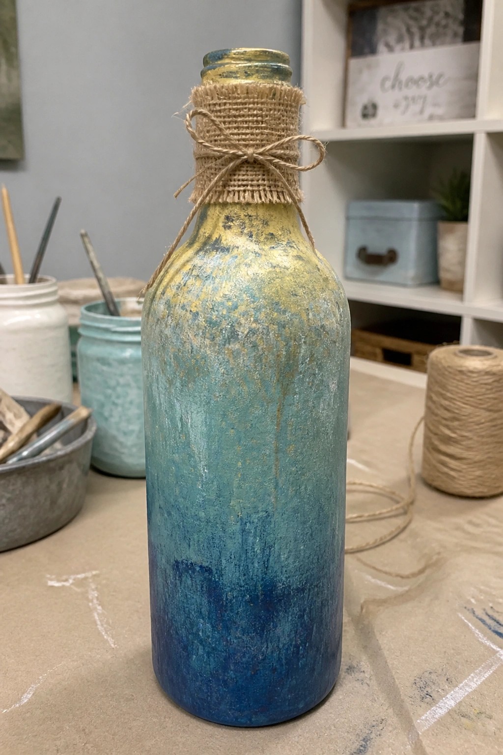 Blue and gold painted bottle with burlap and twine around neck in craft studio