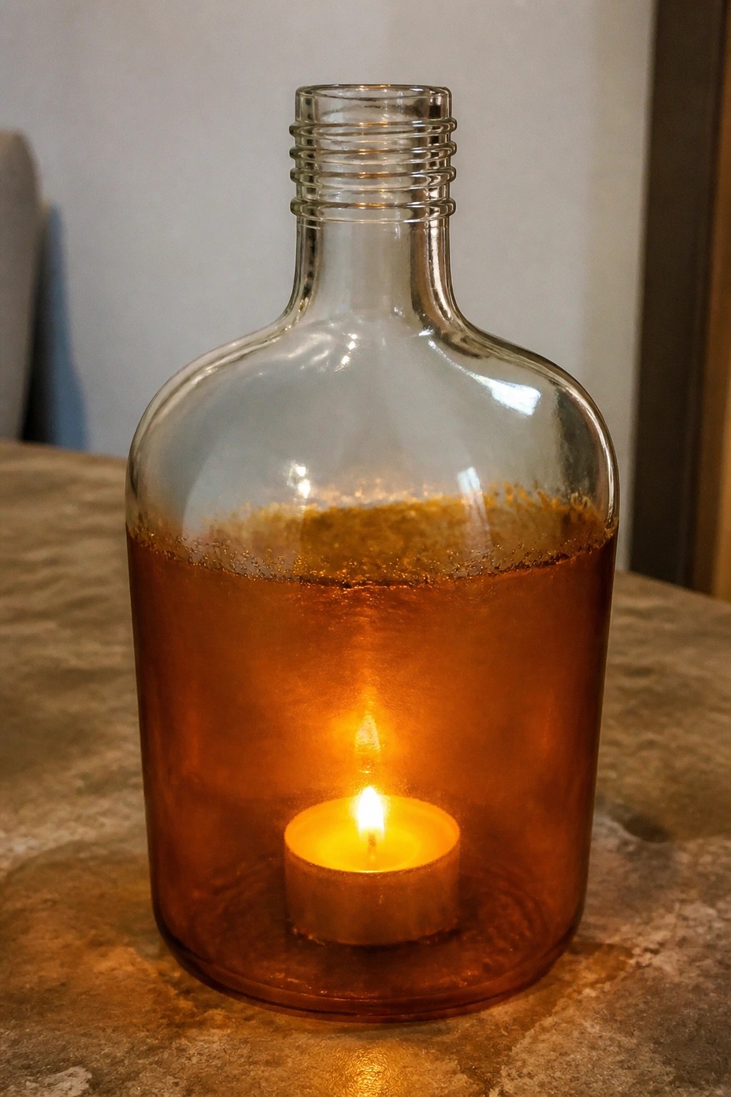 Lit candle flame glowing inside glass bottle with brown liquid residue on table