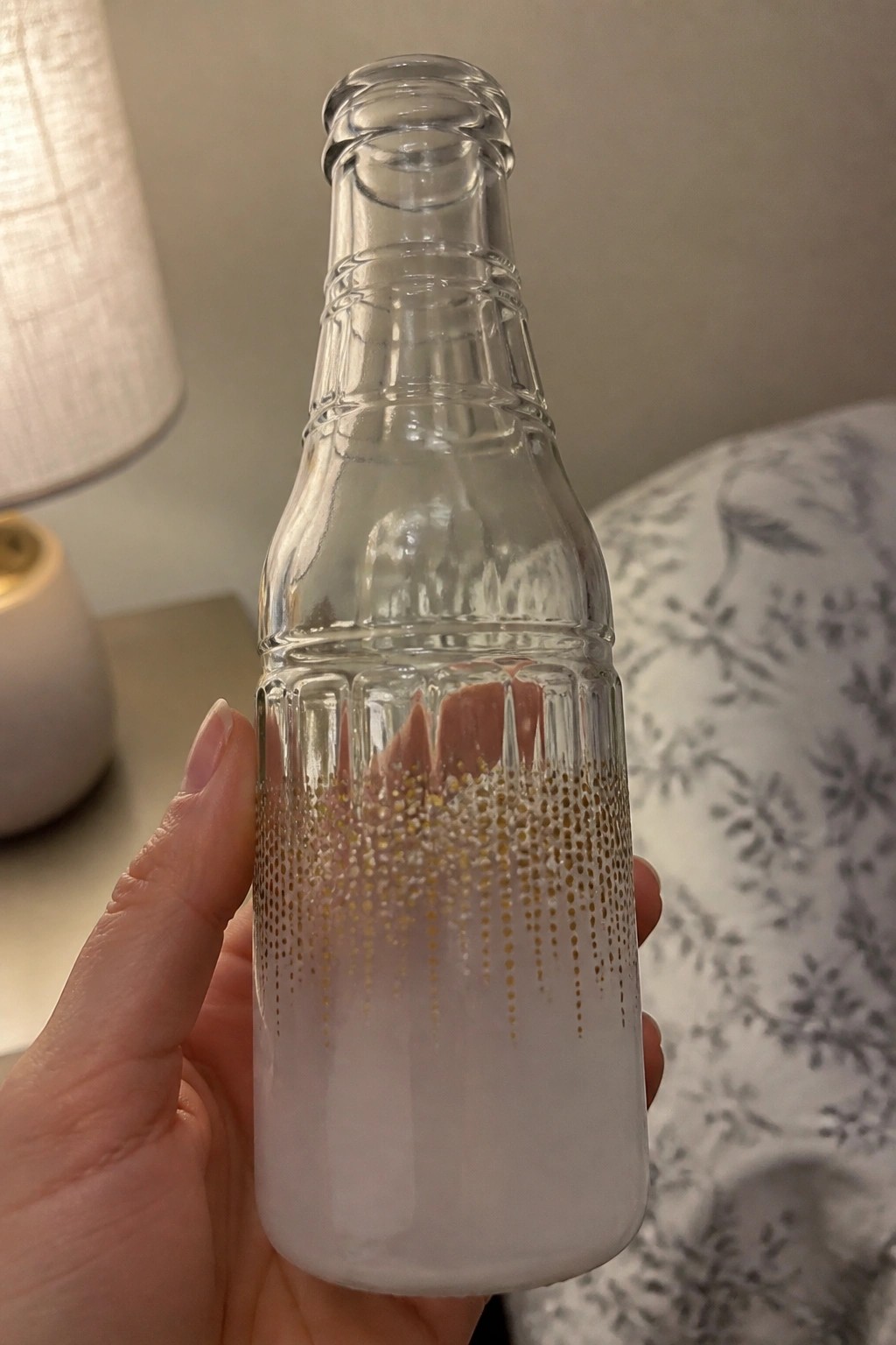 Hand holding clear glass bottle with frosted white base and gold glitter pattern
