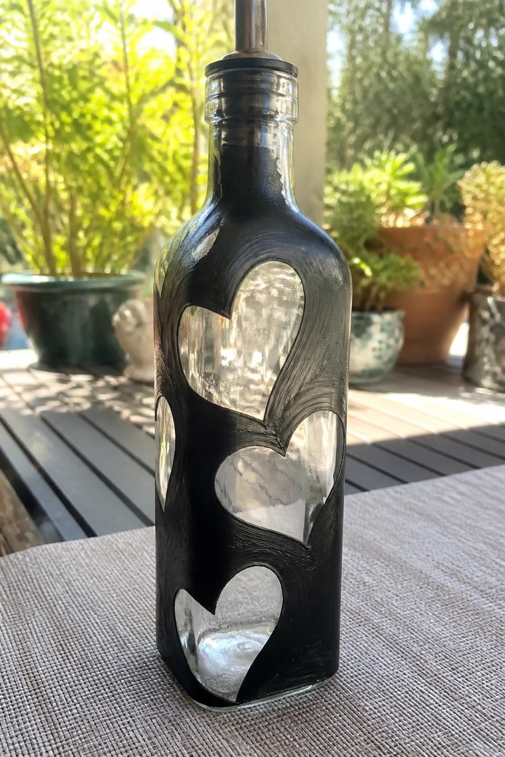 Black glass bottle with heart cutouts and metal pour spout on table