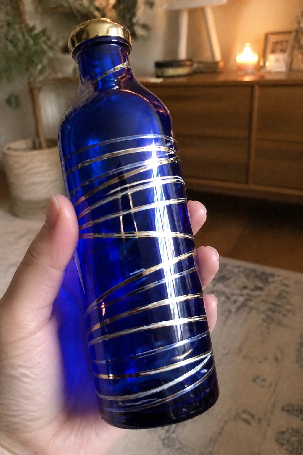 Hand holding cobalt blue glass bottle with spiraling gold stripes and cap