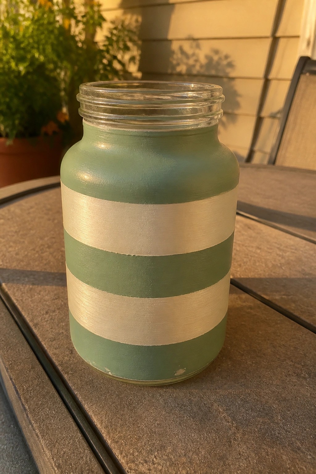 Sage green jar with silver stripes on wooden patio table at sunset