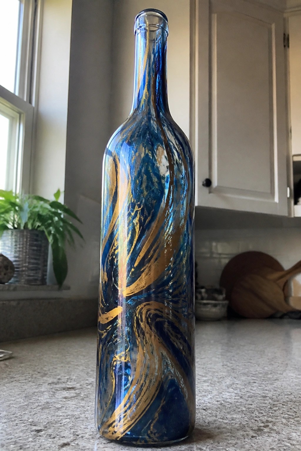 Tall glass bottle with swirling blue and gold paint patterns on kitchen counter