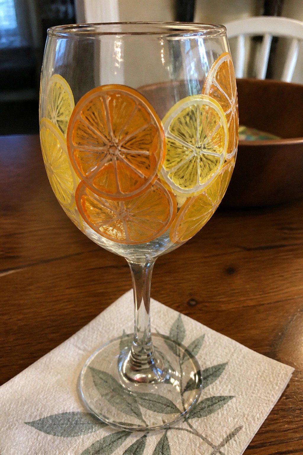Stemmed wine glass with painted orange and lemon slices on leafy paper napkin.