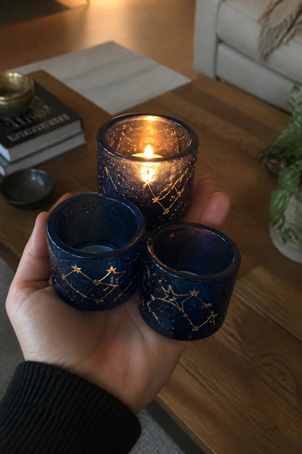 Hand holding three blue glass votives with gold constellations, one candle lit.