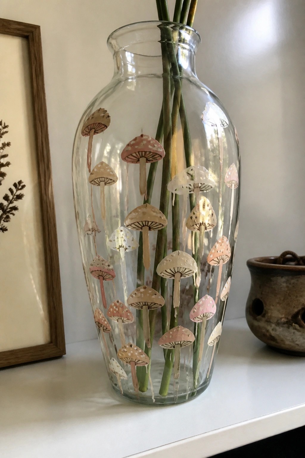 Clear glass vase painted with pink beige mushrooms holding green plant stems