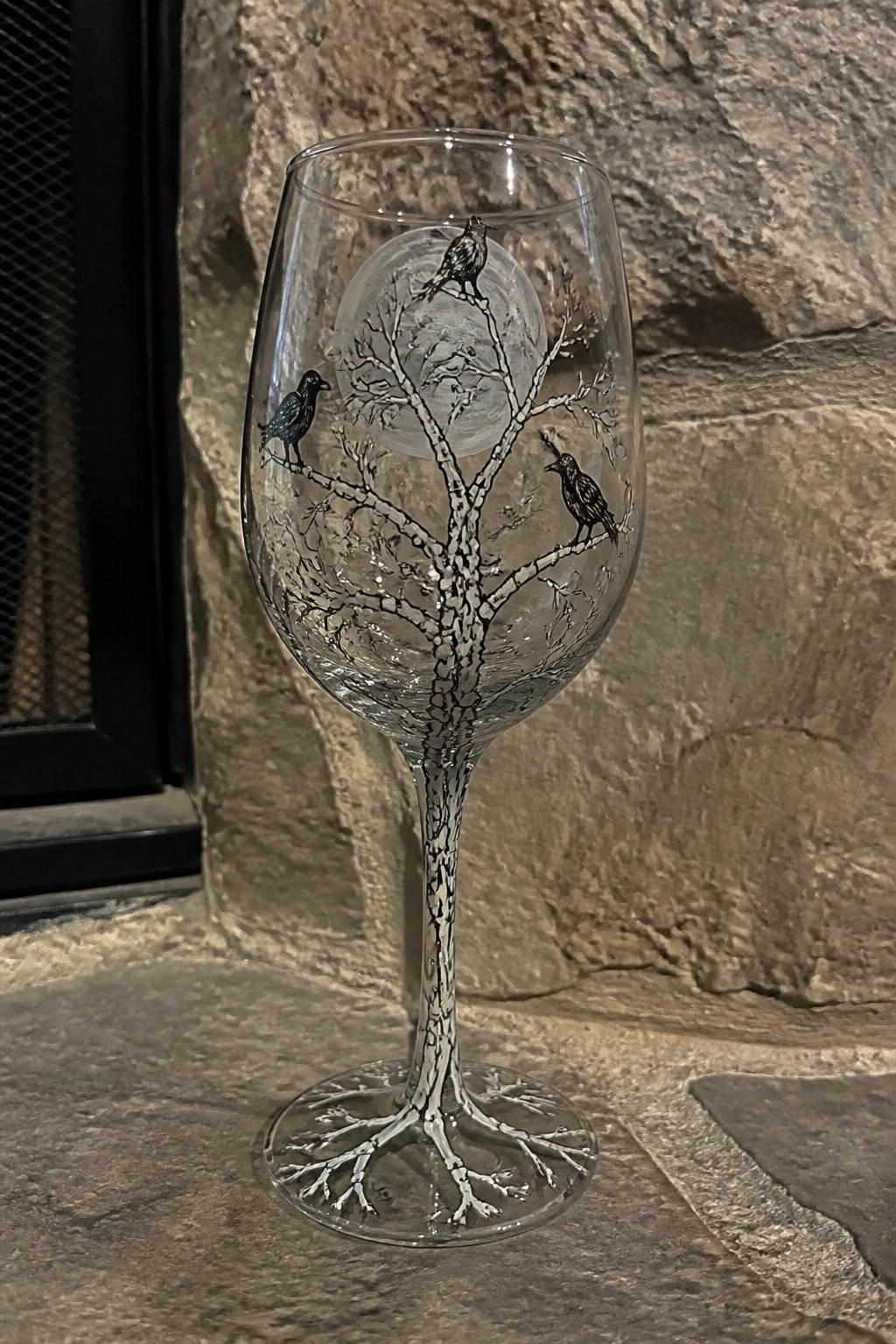 Etched wine glass with bare tree, full moon, and three black birds on stone.