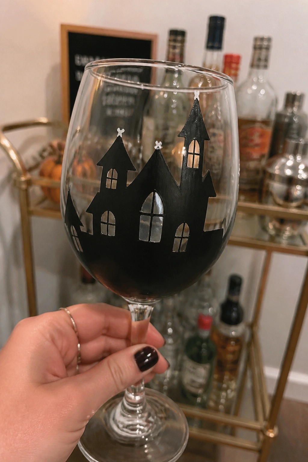 Hand with dark nail polish holding wine glass with black haunted house silhouette